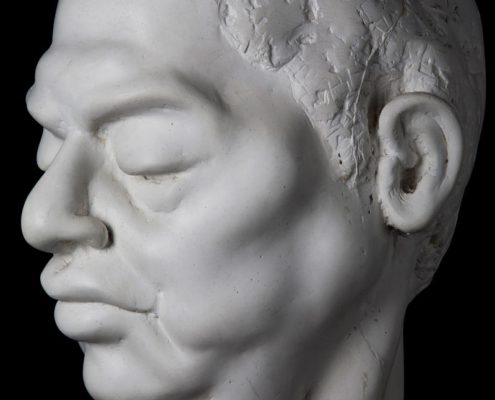 A white sculpture of a man 's head with his eyes closed.