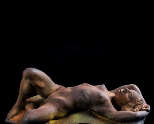 A naked man laying on his stomach in the dark.