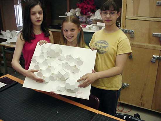 Three girls holding a white board with paper cut outs.