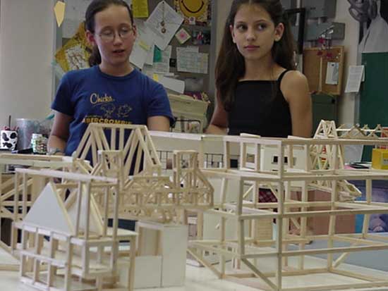 Two girls standing in front of a model building.