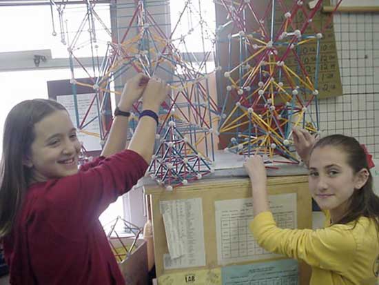 Two girls are playing with a string sculpture.