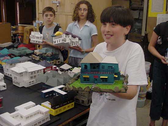 A boy holding a model house in front of other people.