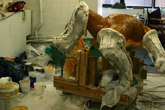 A brown horse standing in the middle of an art studio.