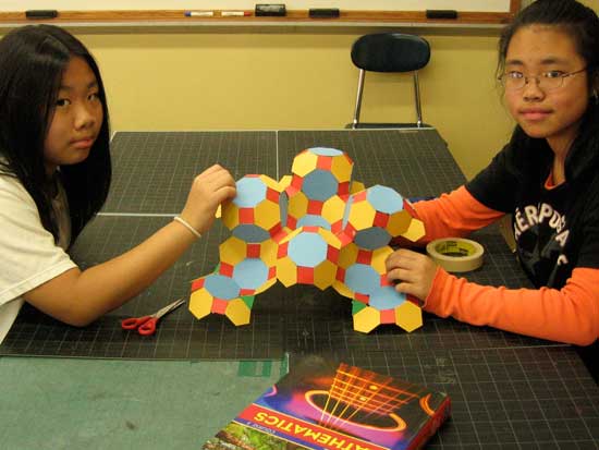 Two children are sitting at a table with a paper robot.