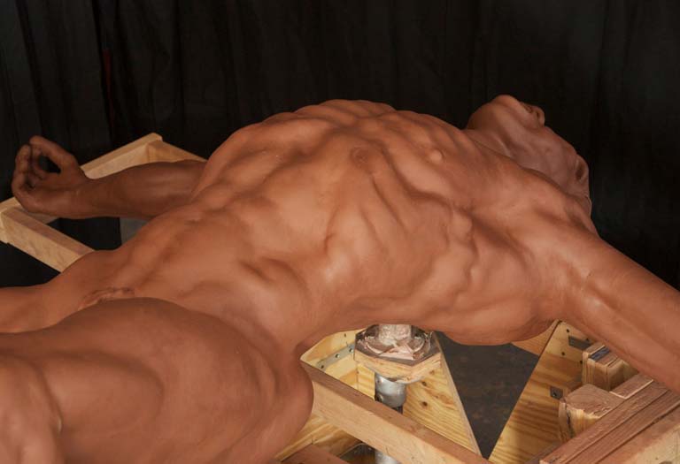 A man with no shirt laying on top of a cake.