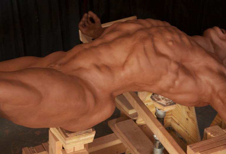 A muscular man is sitting on top of a wooden bench.