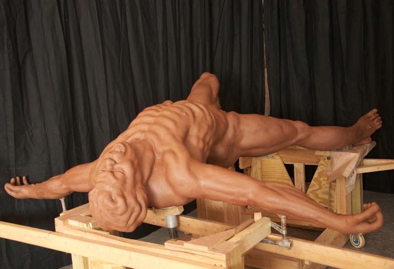 A wooden sculpture of a man laying on his back.