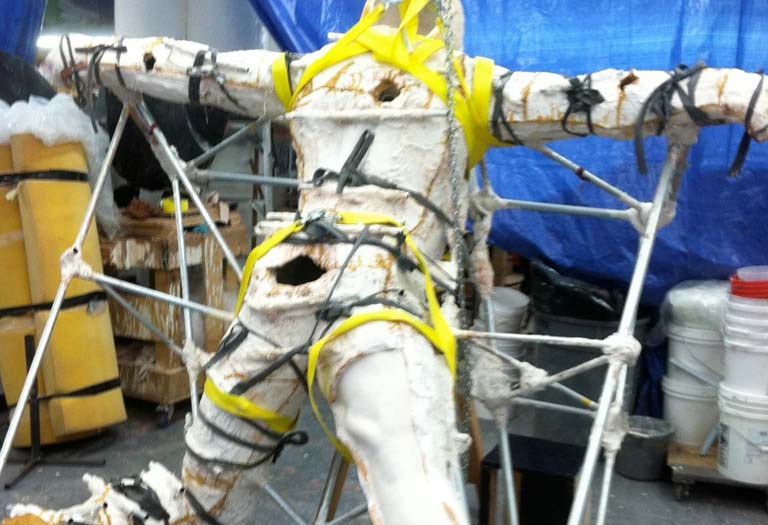 A person in white and yellow outfit hanging from scaffolding.