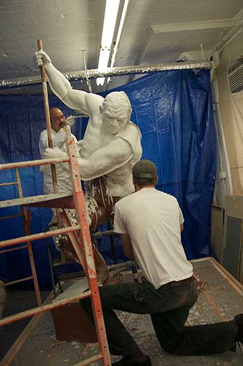 A man in white suit painting a statue.