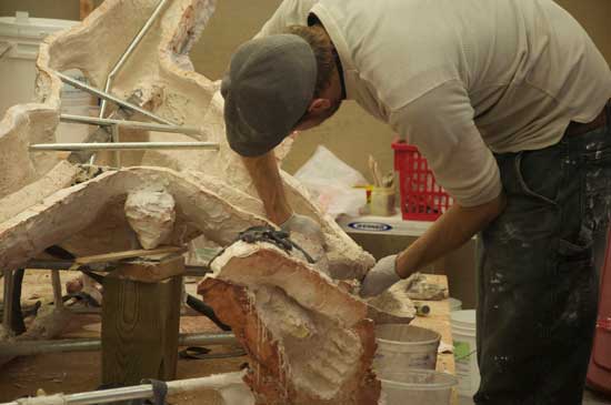 A man in white shirt and hat working on wooden object.