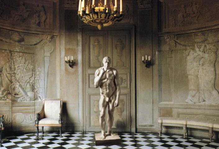 A statue of a man in a room with chairs and a chandelier.