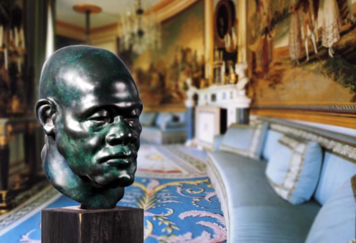 A bust of a man in a room with many paintings.