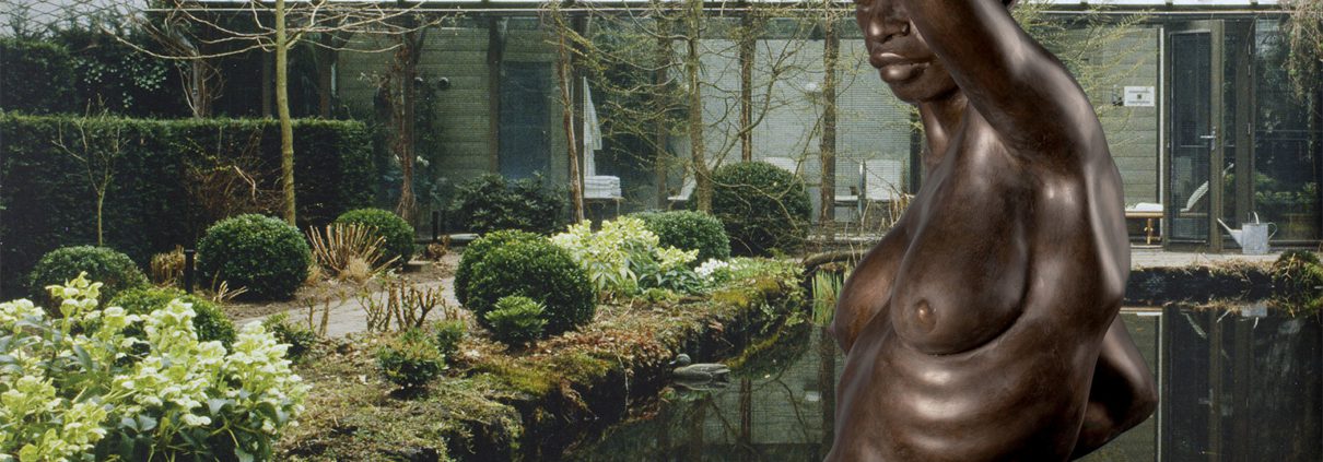 Bronze female torso sculpture beside reflective pond