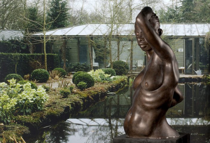 A statue of a woman in front of a pond.